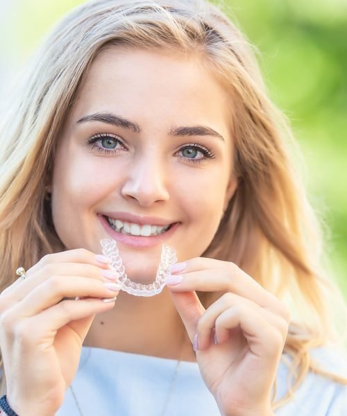 Invisalign orthodontics concept - Young attractive woman holding - using invisible braces or trainer.