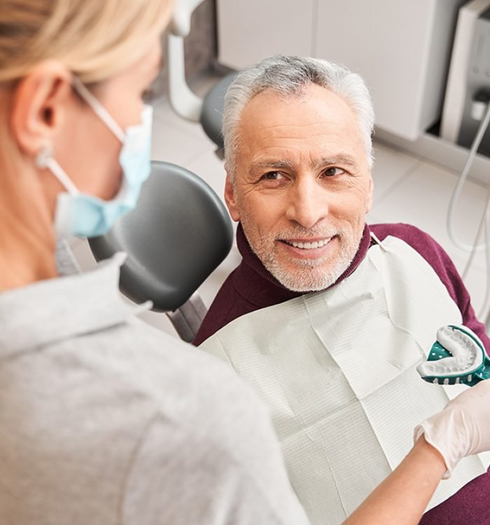 New smile. Back view of the female blonde caucasian doctor presenting dental impression for dentures to the senior smiling man. Stock photo